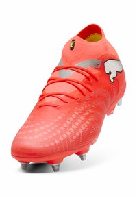 Jasnoczerwony, syntetyczny but piłkarski z teksturowaną cholewką, srebrnymi akcentami i sześcioma formowanymi kołkami zapewniającymi przyczepność.