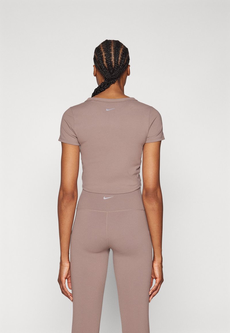 Chemise de sport ajustée marron à manches courtes, assortie à un legging taille haute. Présente le logo Nike discret sur les deux articles.