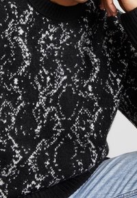 Sweter w czarno-białe wzory, wykonany z teksturowanej dzianiny, z okrągłym dekoltem i ściągaczami przy mankietach.