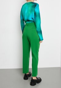 Blouse à manches longues multicolore dans les tons bleu sarcelle avec une texture lisse, associée à un pantalon vert ajusté, doté d'une taille cintrée et de poches.
