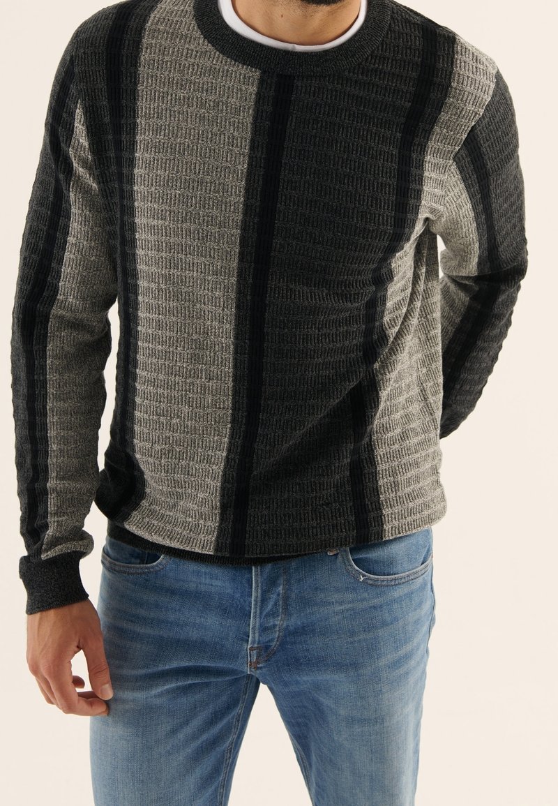 Maglione a maglia texture grigio e nero a righe, con scollo rotondo e dettagli a contrasto sui polsi, abbinato a jeans blu.