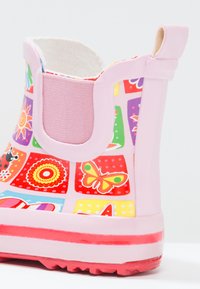Roze rubberen regenlaars met kleurrijke patchworkontwerpen, waaronder vlinders en bloemenpatronen, met een gestructureerde zool en elastische inzet.