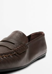 Brown leather loafers featuring a textured finish, stitched detailing, and a flexible sole. Design includes a decorative front flap.
