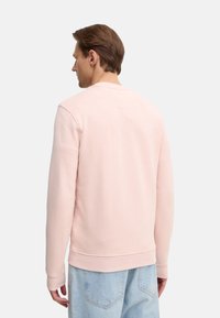 Sudadera rosa con cuello redondo y puños de canalé, que presenta una textura suave y un diseño sencillo, combinada con jeans de color azul claro.