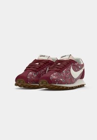 Crvene i uzorkovane atletske cipele od antilopa, bijeli Swoosh logo, smeđa gumena podloga i okrugli vez.