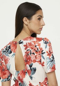Robe fleurie à manches courtes ; base blanche présentant des motifs floraux rouges et bleus ; détail de dos ouvert ; smock à la taille pour un ajustement parfait.
