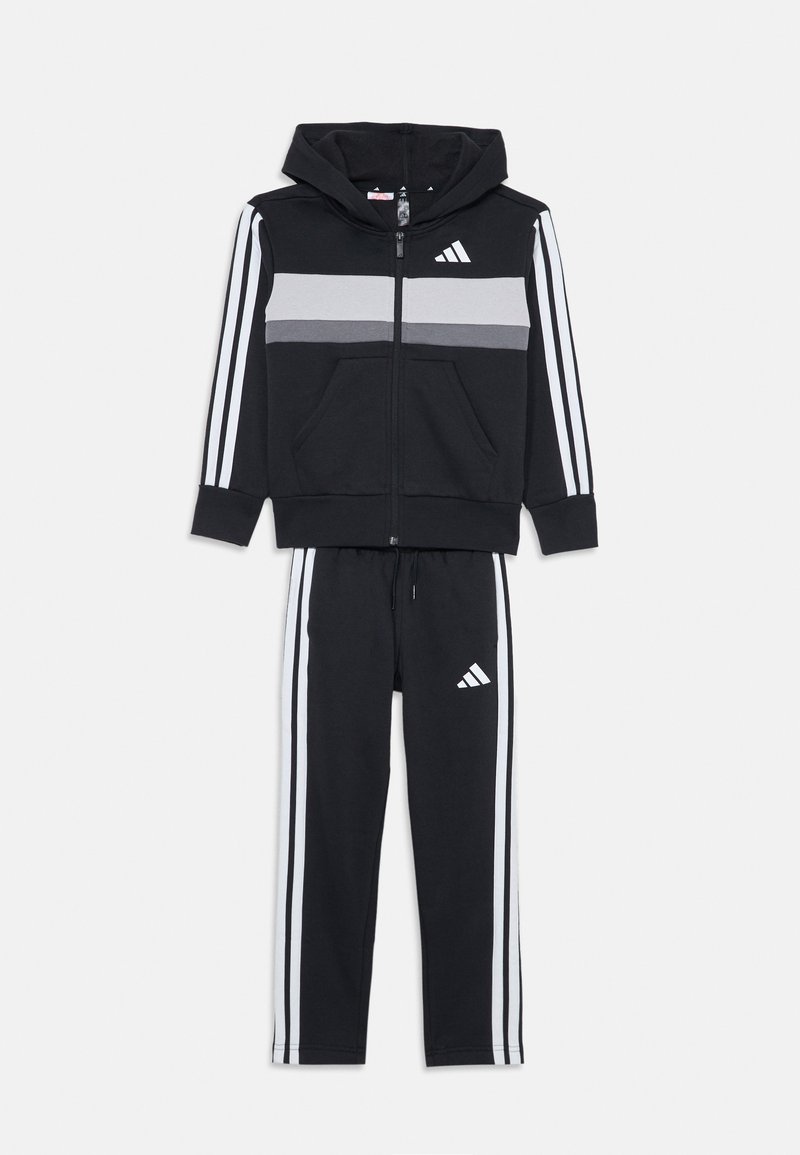 Czarny dres sportowy z rozporkiem na zamek, szary pasek na klatce piersiowej i białe paski po bokach spodni. Zawiera akcenty logo.