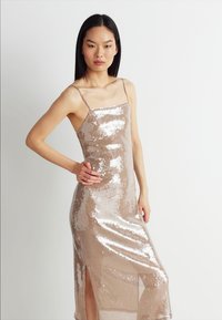Φόρεμα από χρυσό ροζ με παγιέτες, με λεπτές τιράντες, εφαρμοστή σχεδίαση, υψηλό σκίσιμο στα αριστερά και κομψή, λαμπερή υφή.