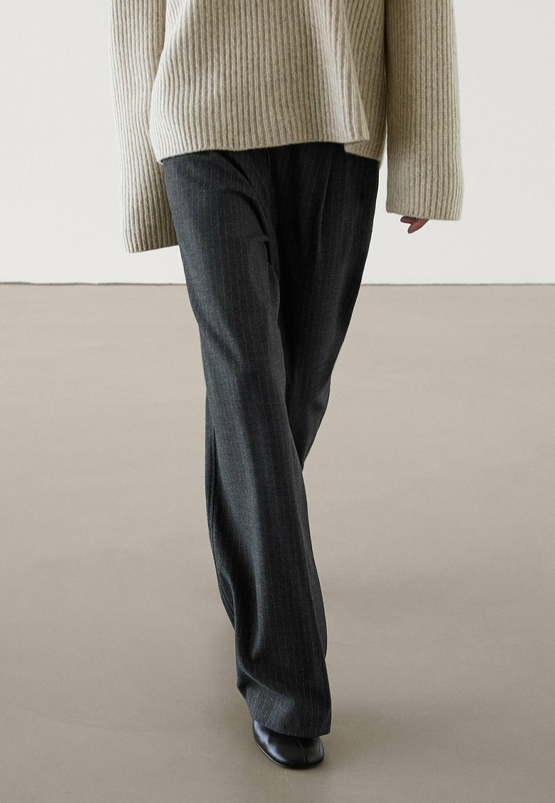 Pantalons gris à rayures fines, coupe ample, associés à un pull à côtes crème. Texture lisse, lignes verticales subtiles et design à jambes larges.