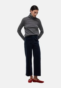 Pull à col roulé gris, pantalon large en corduroy texturé bleu marine et chaussures rouges à enfiler. Design simple et fonctionnel pour une tenue décontractée.