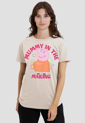 Beige Baumwoll-T-Shirt mit einem Cartoon-Schwein in einem orangefarbenen Kleid, mit dem Text "MUMMY IN THE MAKING" in fetten pinken Buchstaben und floralen Akzenten.