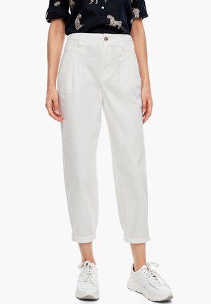 Kvinde iført hvide højtaljede bukser med læg og opbuk ved benene samt hvide chunky sneakers, kombineret med en sort skjorte med dyreprint.