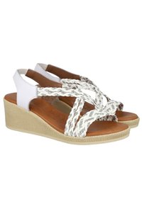 Sandalias cuña con correas trenzadas en blanco y plateado, plantilla de cuero marrón y suela de cuña de fibra natural texturizada.