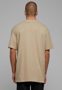 Camiseta de algodón beige con un corte relajado, mangas cortas y cuello redondo. Textura suave, diseño simple sin patrones ni gráficos.