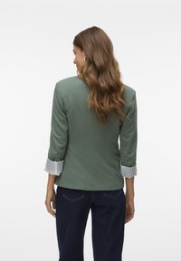 Groene blazer met een getailleerde pasvorm en opgerolde gestreepte mouwen. Gladde textuur en gestructureerd ontwerp. Gecombineerd met donkere jeans voor contrast.