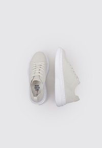 Zapatillas beige con parte superior de tela texturizada, suela de goma blanca y cordones tradicionales. Presenta la frase "Porque no hay un planeta B" en su interior.