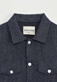 Chemise bleu marine à boutons avec un tissage texturé, col évasé, deux poches avant et boutons argentés. Étiquette indiquant "FRILIVIN, Taille S."