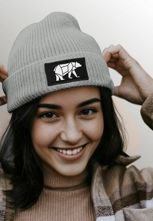 Gray ribbed knit beanie with a black rectangular patch featuring a white geometric bear design. Soft texture, form-fitting shape.