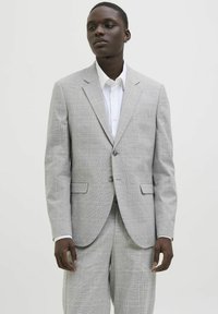 Chaqueta de traje de cuadro gris claro con solapas de muesca, cierre de un solo botón y dos bolsillos frontales, combinada con una camisa de vestir blanca.