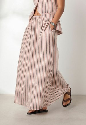 Frau trägt rosa-weiß gestreifte weite Hose mit Vertikalstreifen und passendes ärmelloses Oberteil, läuft barfuß und trägt eine schwarze Uhr am Handgelenk.