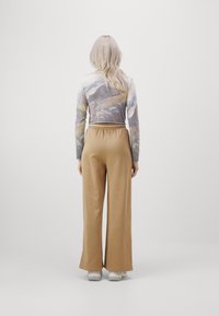 Camiseta de manga larga con estampado de paisaje, combinada con pantalones anchos beige. Tejido suave y corte relajado, complementado con zapatillas de color claro.