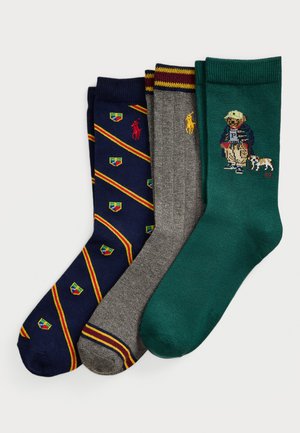 Drei Paar gefaltete Socken: marinblau mit roten und gelben Streifen sowie Wappenlogos, grau mit burdeosfarbenen und gelben Streifen und Logo, grün mit Bären- und Hundedesign.