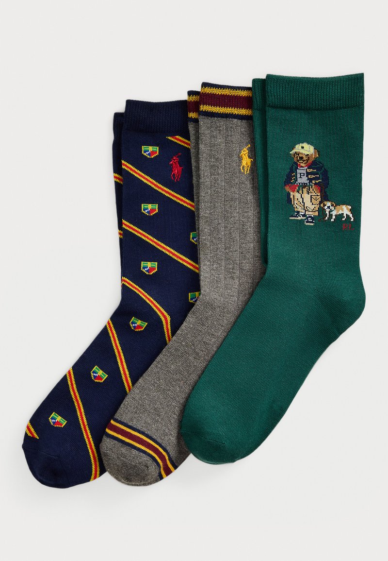 Tri para zloženih nogavic: mornarsko modre z rdečimi in rumenimi črtami ter krovnimi logotipi, sive z burdeos in rumenimi črtami ter logotipom, zelene z obliko medveda in psa.