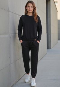 Svart sweatshirt och jogger-set i mjukt tyg, med rund halsringning, ribbstickade muddars och elastisk midja med fickor, tillsammans med vita sneakers.