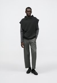 Black hooded sweatshirt with short sleeves, paired with gray tapered trousers and black shoes. Smooth fabric textures and minimalist design.