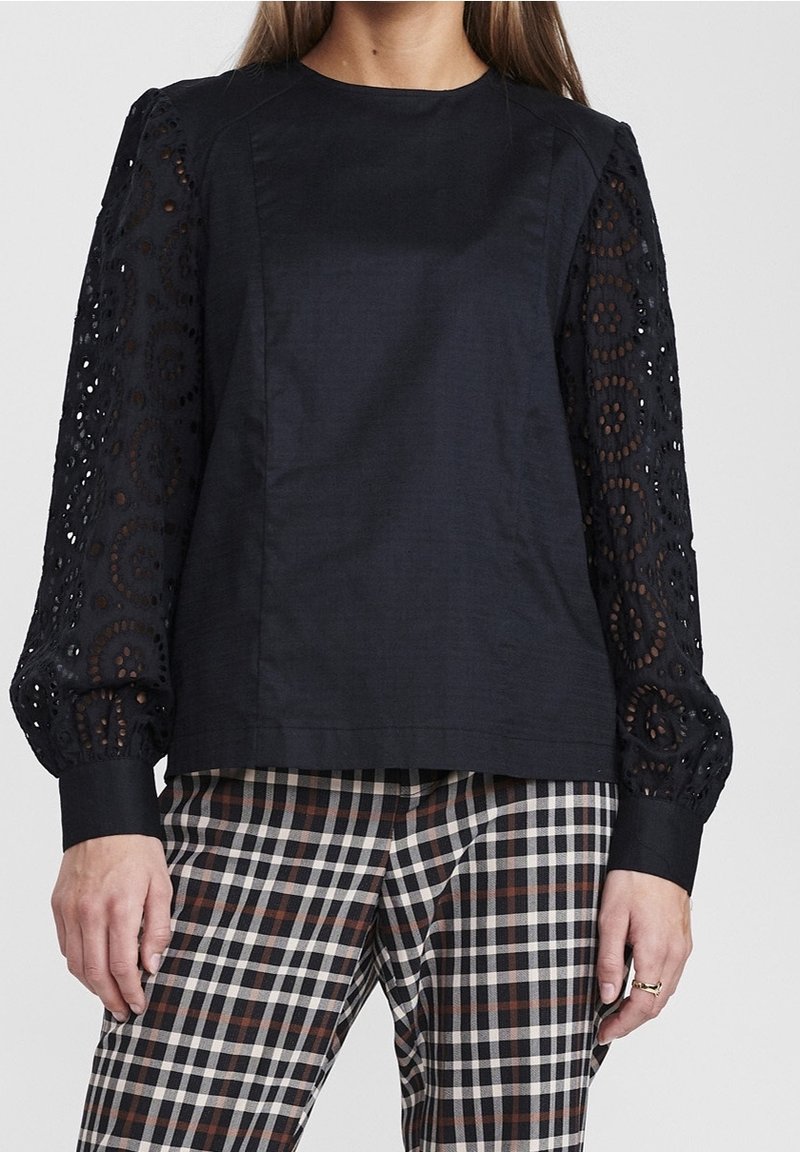 Top nero con maniche lunghe a sbuffo caratterizzate da un intricato dettaglio in pizzo. Abbinato a pantaloni a quadri in nero, bianco e marrone. Tessuto liscio.