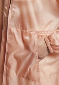 Ljusrosa, glänsande tygjacka med en sidoficka och elastiska ärmmuddar, med ett subtilt rutmönster och rena sömmar.