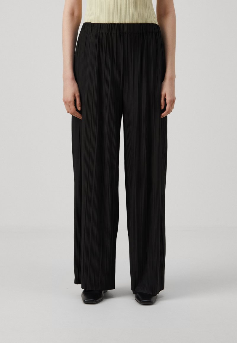 Black pleated trousers with an elastic waistband and wide legs, made from a lightweight fabric. Features subtle vertical texture and a loose fit.