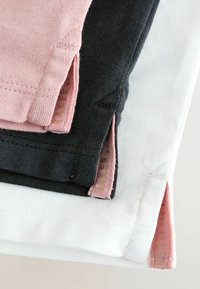 Tre t-shirt piegate in rosa, nero e bianco. Ognuna ha delle fessure laterali con un tessuto interno a contrasto, che mostra una morbida texture a maglia.