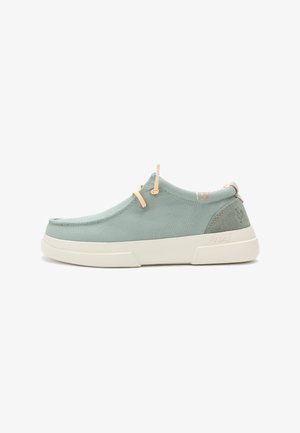 Des baskets à enfiler en toile bleu clair avec une semelle en caoutchouc blanc. Présentent des sangles en tan et un subtil detailing au niveau du talon arrière. Texture lisse.