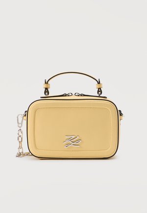 Obdélníková měkká žlutá kabelka s krátkým madlem, stříbrným řetízkovým popruhem, dvojitým zipem a stříbrným stylizovaným logem „KL“ na předním panelu.