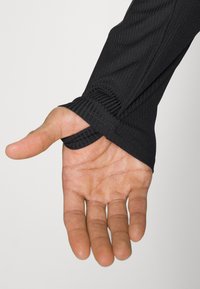 Schwarzes Langarmkleidungsstück mit gerippten Bündchen, das eine Hand durch ein Daumenloch zeigt; glatte Textur mit taillierter Passform.