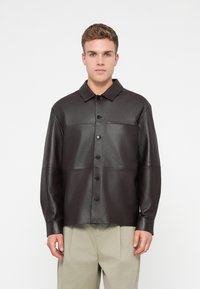 Fekete bőr ingdzseki gombos elülső résszel, galléros nyakkal és hosszú ujjakkal. Paneles kialakítással és laza szabással rendelkezik.