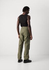 Cargo-Hosen in Olivgrün mit elastischem Bund, Seitentaschen und schmal zulaufenden Beinen. Das Model trägt ein enges schwarzes Tanktop und Sneakers.