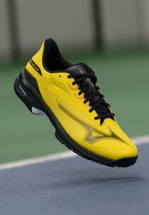 Yellow athletic shoe with a sleek design, featuring a black lacing system, textured upper, and a thick rubber sole for traction.