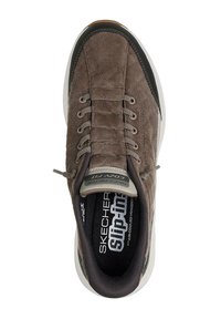 Zapatilla deportiva de pana marrón con superficie texturizada, diseño con cordones, puntera reforzada y detalles en negro. Logo visible en la plantilla.