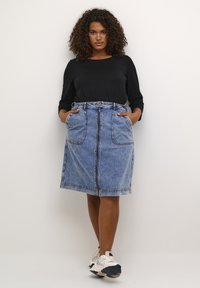 Jupe A-line en denim avec une fermeture éclair à l'avant, des passants de ceinture et deux grandes poches avant. La jupe est bleu clair et arrive au genou, avec un design décontracté.