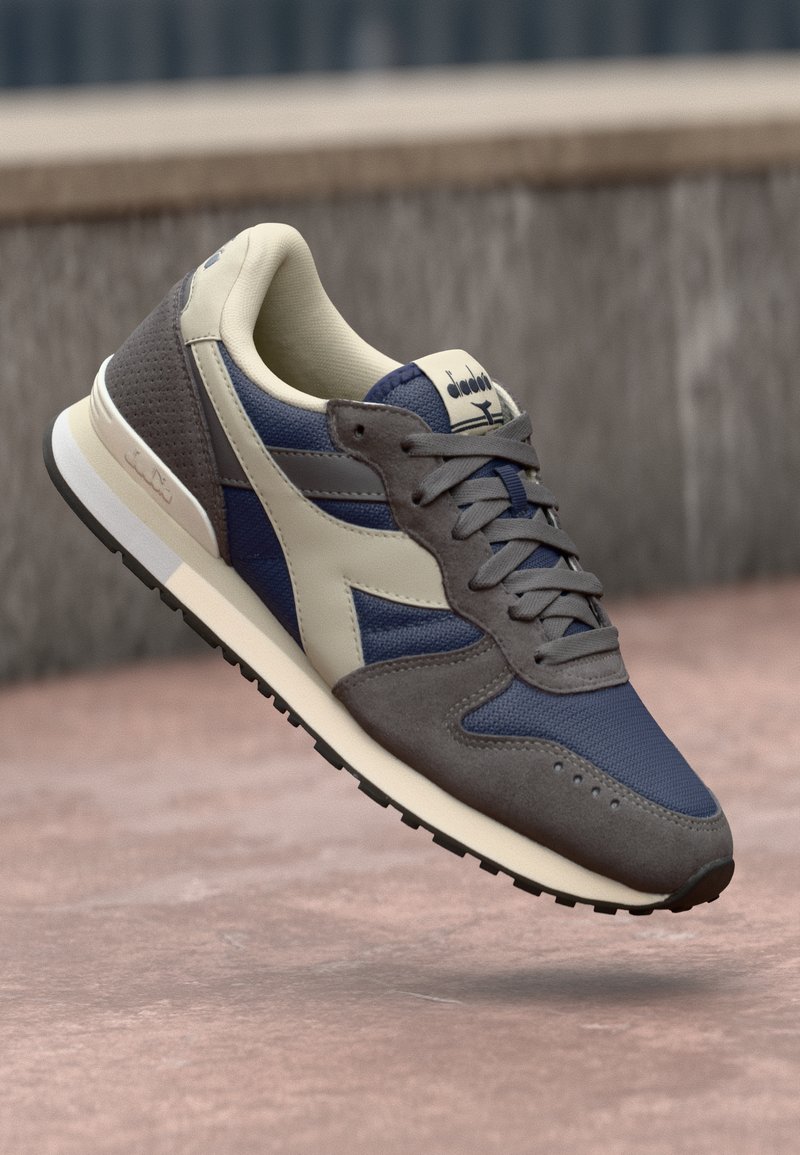 Scarpa da corsa da uomo caratterizzata da una combinazione di mesh blu navy e suede grigio, con dettagli in pelle beige. Design classico con allacciatura e suola in gomma nera.