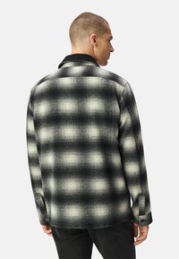 Camicia a quadri in tonalità nere e grigie, caratterizzata da un colletto con bottoni, maniche lunghe e un tessuto con texture dal taglio squadrato.