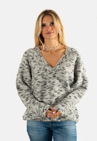 Suéter de punto en gris y blanco con escote en V, puños y dobladillo acanalados. Presenta un corte holgado y un patrón texturizado en toda su extensión.