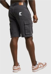 Szürke cargo shorts tartós anyagból, több zsebbel és logóval a hátsó zsebben. Világos sportcipővel viselve.