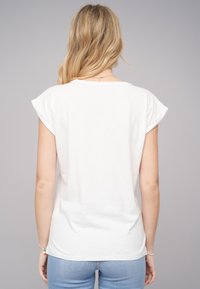 T-shirt en coton blanc avec des manches courtes enroulées, coupe décontractée, col rond et texture lisse. Présente un dos uni sans motifs ni accents.