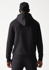 Μαύρο φούτερ με κουκούλα σε εφαρμοστή γραμμή, με απαλή υφή και μεγάλη κουκούλα. Μανσέτες και τελείωμα με ριμπ ύφασμα και μινιμαλιστικό στιλ.