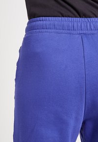 Paarse sportieve broek met een geribde tailleband en een gladde textuur. Zijzakken zijn zichtbaar, zonder extra patronen of accenten.