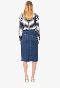 Gonna a tubino in denim con vita alta, due tasche posteriori e orlo che arriva sotto il ginocchio, abbinata a una blusa a righe in bianco e nero.