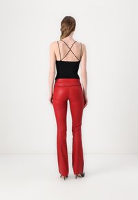 Black tank top with crisscross straps at the back paired with red fitted leather flared pants and black high-heeled shoes.